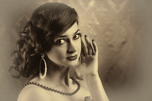 Woman dressed in Roaring twenties era with feathers boa on dark background. Retro, party, fashion concept. Sepia film effect. High quality photo