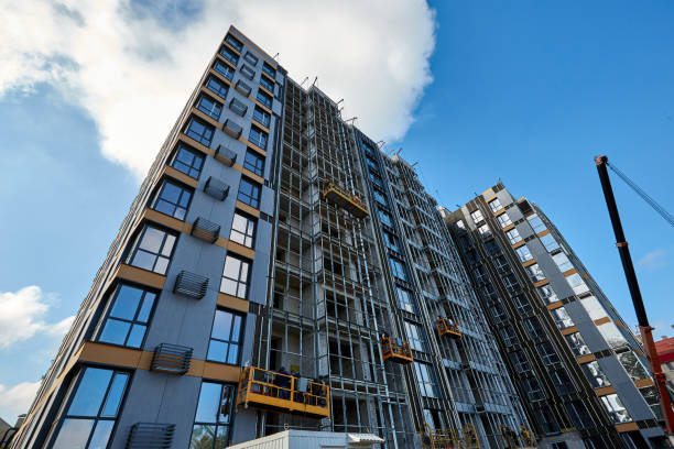 istock Modern new building under construction against blue sky. Builders working in suspended construction cradles on the facade. Crane machine is nearby 1319172896