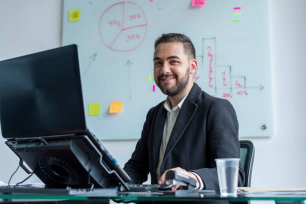 Man working in an office on his laptop Latino ethnic man between 25-35 years old is working in an office on his laptop in times of COVID-19 latin script stock pictures, royalty-free photos & images