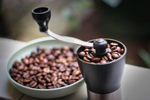 roasted coffee beans and a coffee grinder coffee beans in a cup and in a coffee grinder on the porch of the house in the afternoon coffee grinder stock pictures, royalty-free photos & images