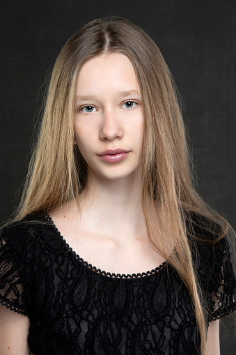Beautiful teenager girl with long hair on a gray background. A girl with a European face type.