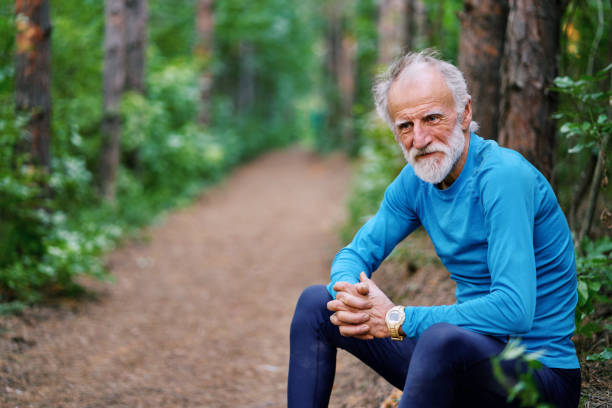 Tired elderly athlete taking a break after long workout in the forest