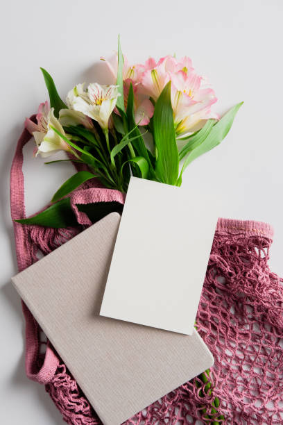 istock String grocery bag with flowers, paper notebook and blank paper card on white background. Flat lay, top view. Summer fashion concept. 1319178194