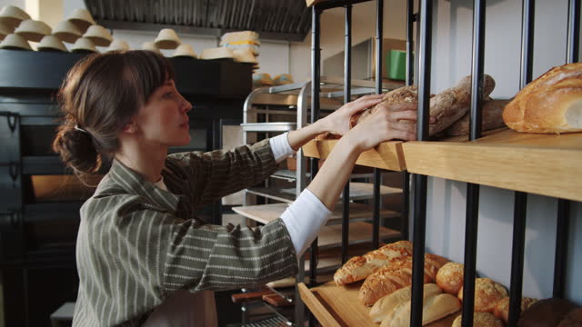 Woman Putting Fresh Bread on Display Rack in Bakery