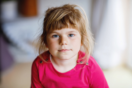 Portrait of happy smiling toddler girl indoors. Little preschool child with blond hairs looking at the camera