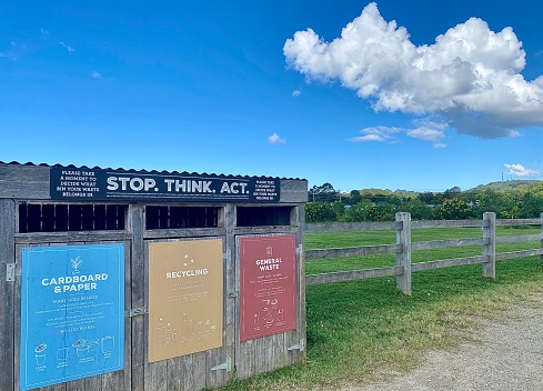 Horizontal of recycling waste rubbish bin for environmentally responsible way in public grass area with tree lined horizon and white fluffy cloud blue sky in country NSW Australia