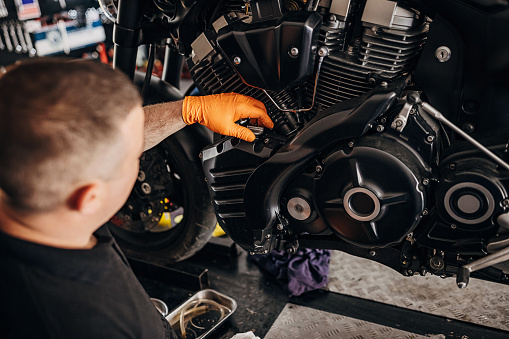 One man, male motorcycle mechanic changing oil on motorcycle, in his workshop.