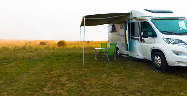 la maison mobile ist restant sur la pelouse verte. chaises pliantes vides et table sous la verrière près de la nouvelle remorque moderne de remorque de véhicule de récréation. concept de tourisme et de vacances. - motor home park camping luxury photos et images de collection