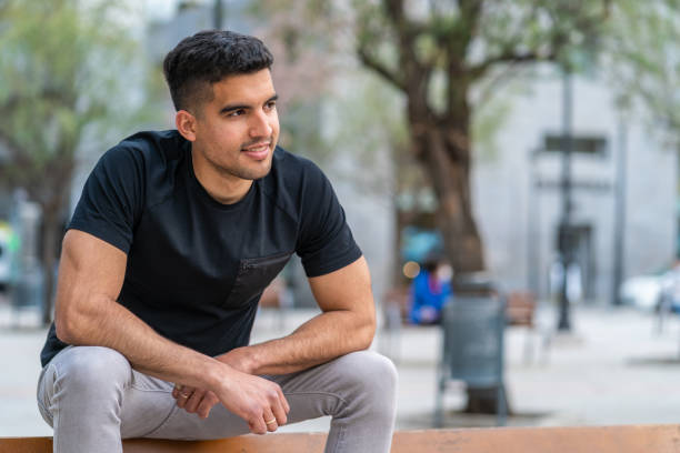 Hispanic young man sitting on a bench in the city stock photo