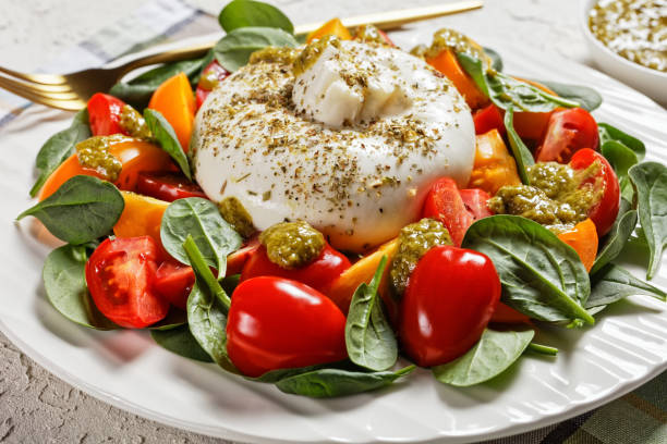 primer plano de espinacas, tomate y ensalada de queso burrata con aderezo pesto de albahaca en un plato blanco, cocina italiana - mozzarella caprese salad tomato italian cuisine fotografías e imágenes de stock