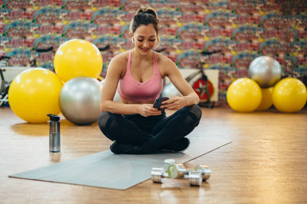 młoda atrakcyjna kobieta za pomocą smartfona na siłowni - high peaks audio zdjęcia i obrazy z banku zdjęć