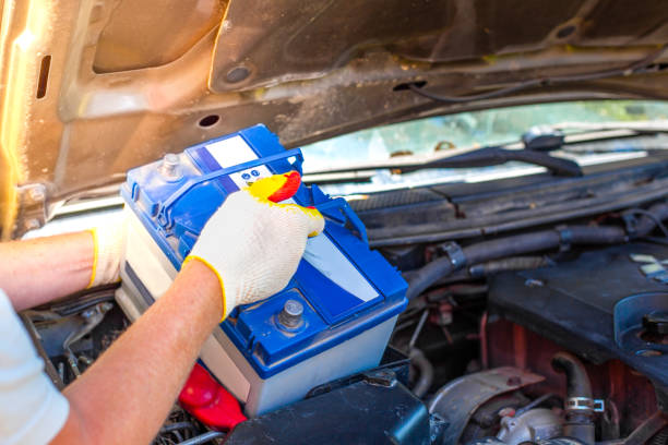 maintenance of the machine. a male car mechanic takes out a battery from under the hood of a auto to repair, charge or replace it - car battery imagens e fotografias de stock