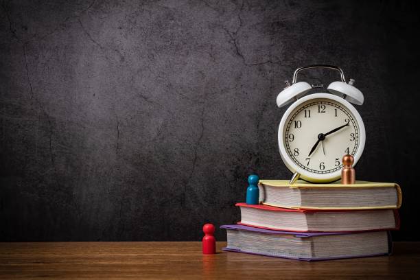 istock Learning, education concept. Alarm clock and a stack of books on the desktop. The blank space is for the title or text. 1319206414