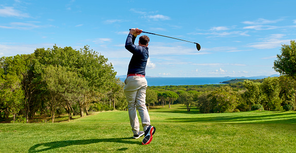 Handsome older Caucasian golf player strolling down the golf course, carrying his golf bag and smiling