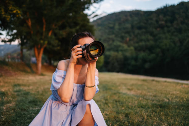 A beautiful young modern woman in blue dress with slit taking photos with camera