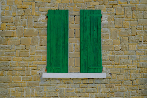 Closed window with green shutters in the brick wall. Building exterior background.