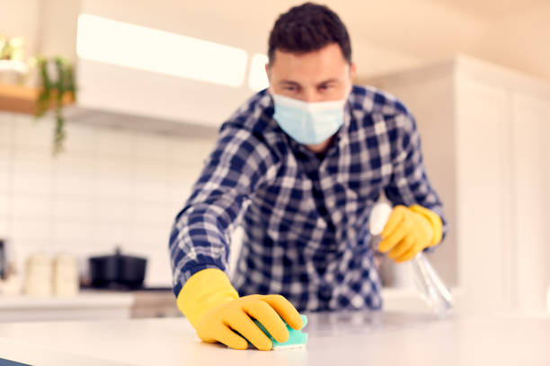 istock Man At Home Wearing Mask In Kitchen Doing Housework And Cleaning Counter Surface With Spray 1319228277