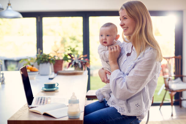 istock Working Mother Using Laptop At Home Whilst Holding Smiling Baby Son On Knee 1319228747