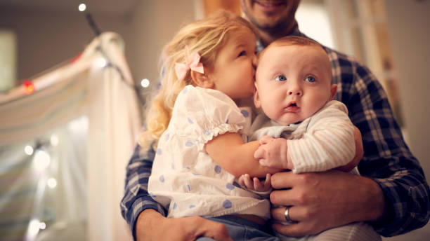 primer plano de la niña abrazando a su hermanito mientras está sentado en la rodilla del padre en casa - 2 5 meses fotografías e imágenes de stock