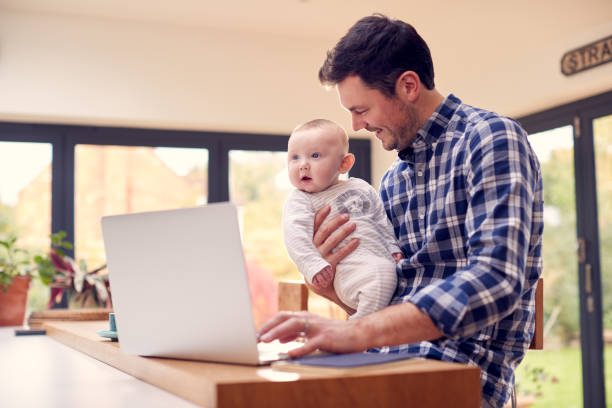 istock Working Father Using Laptop At Home Whilst Holding Smiling Baby Son On Knee 1319230446