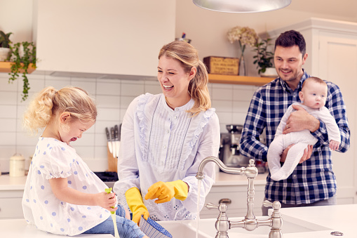 Familia sonriente divirtiéndose en la cocina lavando en el fregadero juntos photo