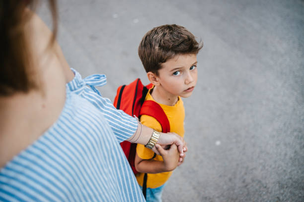 Mother holding her son's hand sending him to school A son with a backpack and his mother holding his hand sending him to school on the first day of school and the schoolboy is looking at the camera worried mom with kids stock pictures, royalty-free photos & images
