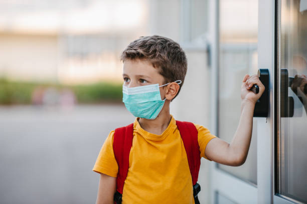 istock Schoolboy with the mask on opening school door 1319230848