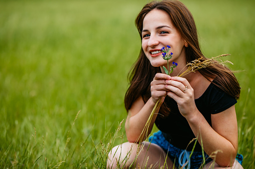 Portrait of pretty young Caucasian woman crouching in grass.