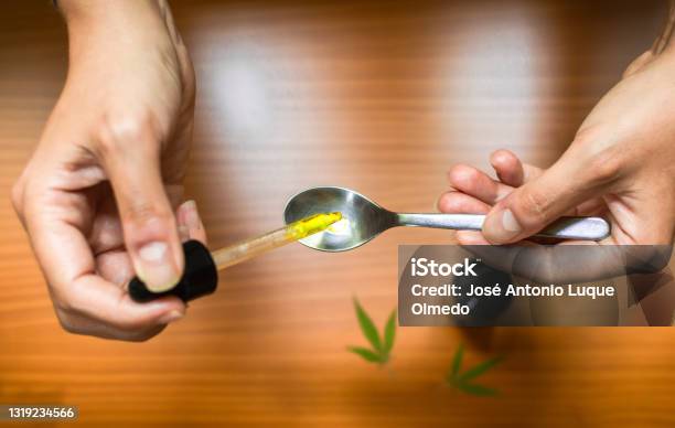 Top View Of Hands Pouring Drops Of Cbd Oil Into A Spoon To Calculate The Dosage Using Cannabis Oil Stock Photo - Download Image Now