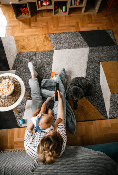 Mother and daughter having fun watching tv Young woman and her baby girl watching kids tv show at home in a company of a poodle dog. Sitting on the floor, changing tv channels poodle color image animal sitting stock pictures, royalty-free photos & images