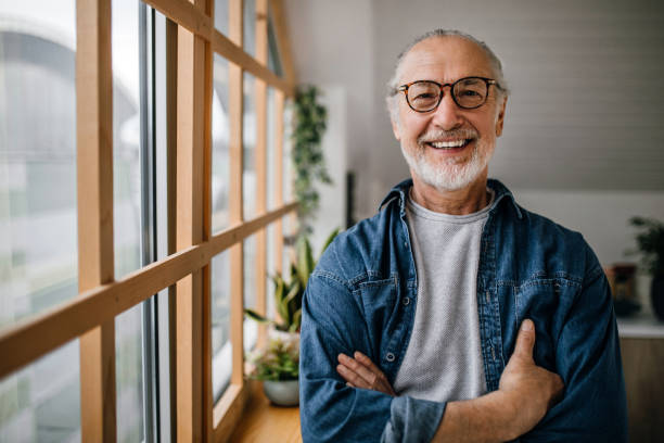 Portrait of handsome senior man standing next to the kitchen window Portrait of handsome active senior man standing next to the window, looking at camera, smiling. 60 69 years stock pictures, royalty-free photos & images
