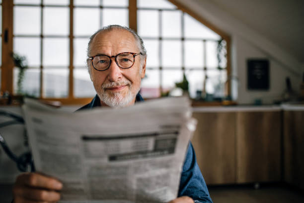 homme aîné à la maison affichant des journaux - reading newspaper men magazine photos et images de collection