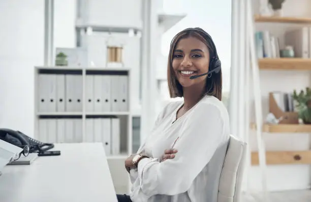 Photo of Shot of an attractive young businesswoman sitting alone in her office with her arms folded and wearing a headset