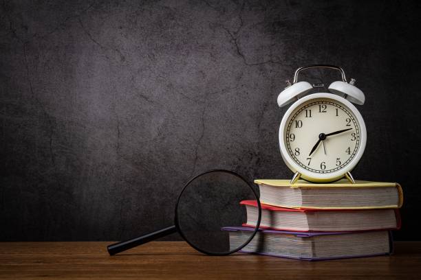 istock Learning, education concept. Time management concept. Alarm clock with stacked books  and magnifying glass on the desktop. Blank space for your title or text. 1319247521