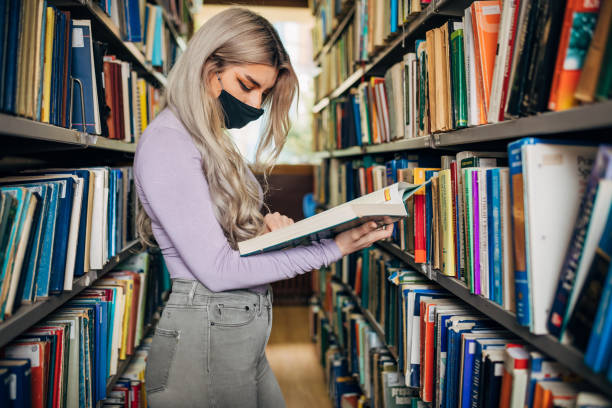 istock Curious University student seeking for a textbook at University library, while wearing protective face mask as a new normal 1319250614