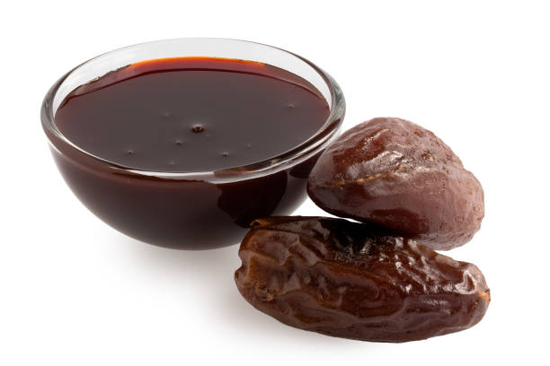 Dry dates and date syrup Date syrup in a glass bowl next to two whole dry pitted dates isolated on white. date syrup stock pictures, royalty-free photos & images