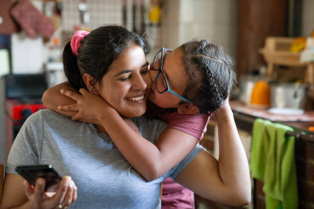 Loving girl kissing her mother while she's checking her cell phone at home