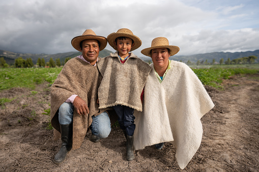 Latin American family farming in their land wearing ruanas and hats and looking happy â agricultural lifestyle concepts