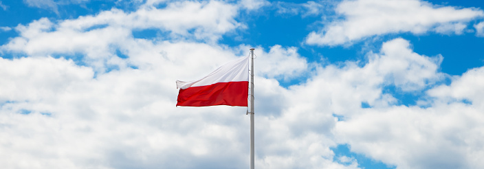 Poland flag waving in the wind in the blue sky. Polish white-red flag in the clouds.