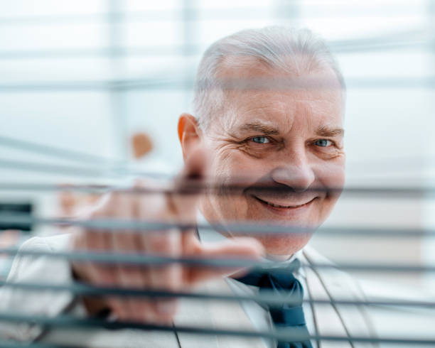 istock smiling successful businessman looking through the blinds 1319257838