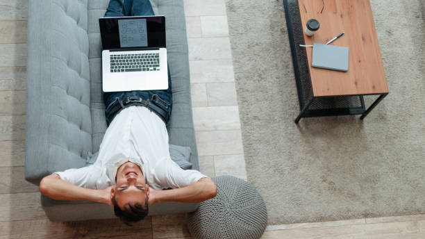 istock happy man with a laptop lying on the couch 1319257977