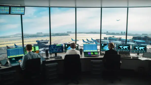 Photo of Diverse Air Traffic Control Team Working in a Modern Airport Tower. Office Room is Full of Desktop Computer Displays with Navigation Screens, Airplane Flight Radar Data for Controllers.