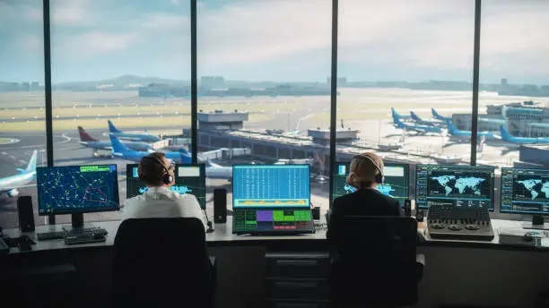 Photo of Diverse Air Traffic Control Team Working in a Modern Airport Tower. Office Room is Full of Desktop Computer Displays with Navigation Screens, Airplane Departure and Arrival Data for Controllers.