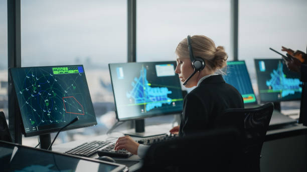 istock Female Air Traffic Controller with Headset Talk on a Call in Airport Tower. Office Room is Full of Desktop Computer Displays with Navigation Screens, Airplane Departure and Arrival Data for the Team. 1319258417