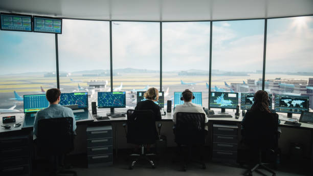 現代の空港タワーで働く多様な航空管制チーム。オフィスルームは、ナビゲーション画面、飛行機の出発とコントローラの到着データとデスクトップコンピュータディスプレイがいっぱいで� - air traffic control tower ストックフォトと画像