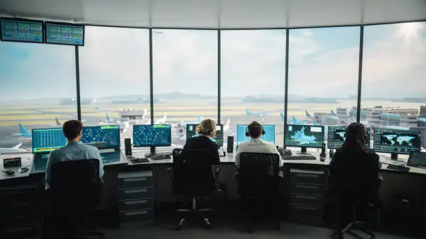 Photo of Diverse Air Traffic Control Team Working in a Modern Airport Tower. Office Room is Full of Desktop Computer Displays with Navigation Screens, Airplane Departure and Arrival Data for Controllers.