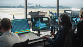 Female Air Traffic Controller with Headset Talk on a Call in Airport Tower. Office Room is Full of Desktop Computer Displays with Navigation Screens, Airplane Flight Radar Data for the Team.