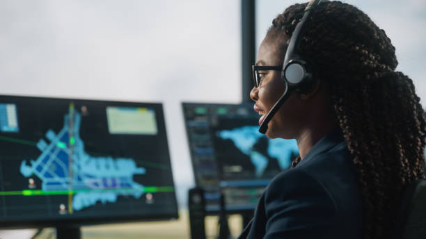 contrôleur de la circulation aérienne féminin avec casque parler lors d’un appel dans la tour de l’aéroport. la salle de bureau est pleine d’écrans d’ordinateur de bureau avec écrans de navigation, données de départ et d’arrivée d’avio - dispatcheur photos et images de collection