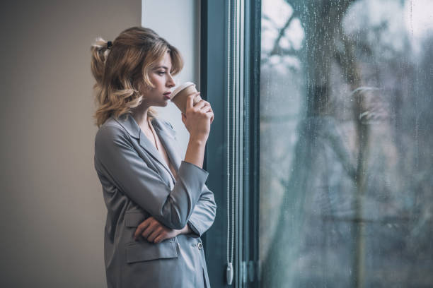 istock Pensive woman drinking coffee standing near window 1319259840