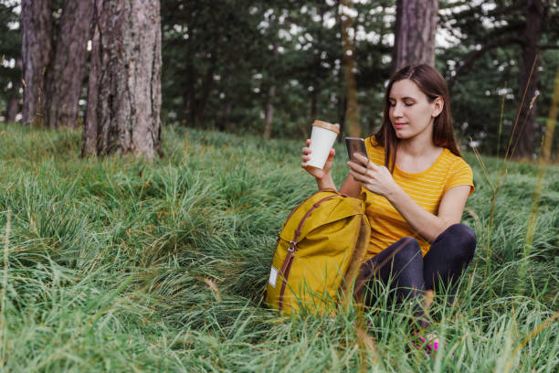 istock Woman in the forest is using mobile phone and holding travel mug 1319259899
